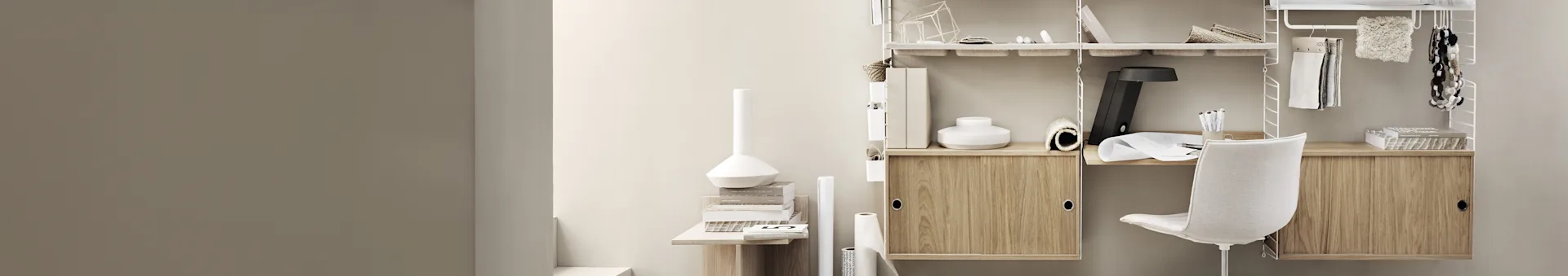 Et minimalistisk hjemmekontor med et hvitt modulært hyllesystem, lyse trekabinett og en hvit kontorstol, fylt med bøker og kontorrekvisita.