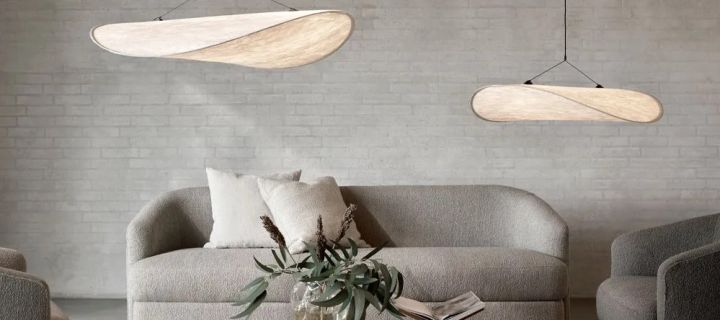 Her ser du to Tense lampeskjermer fra New Works hengende over en grå sofa og stuebord med bøker.