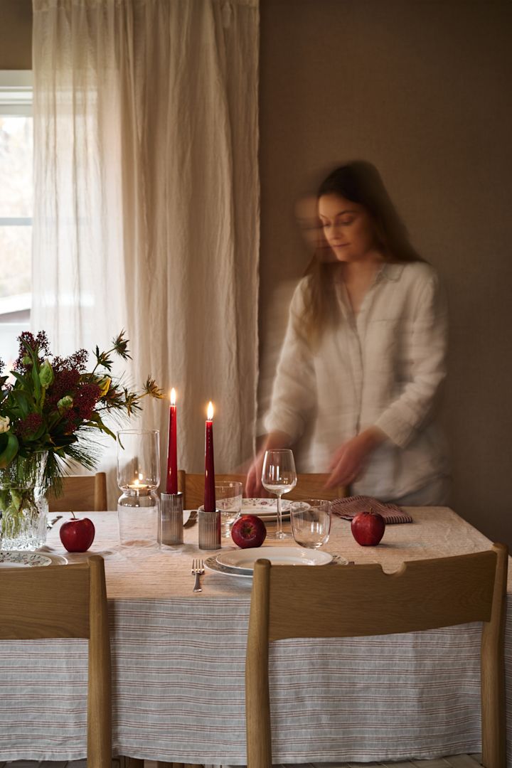 En kvinne dekker et enkelt julebord med røde lys, mønstret juleporselen og en enkel stripete duk. 