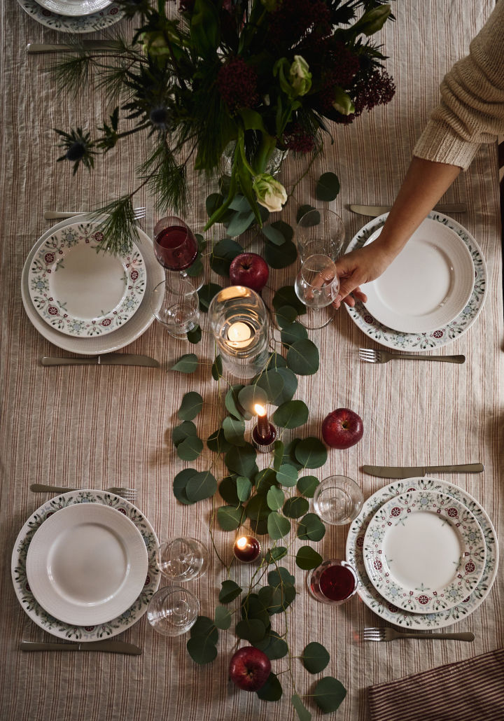 En enkel og elegant idé til juleborddekking fotografert ovenfra med grønne blader og røde epler som dekorasjon. 