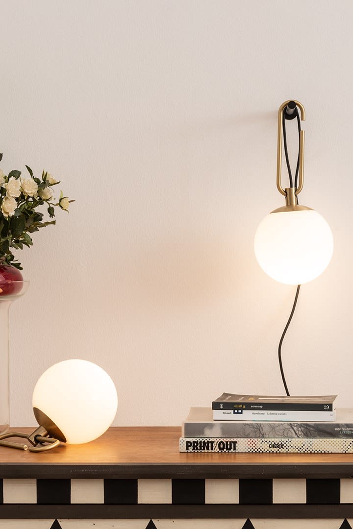 NH vegg- og bordlampene fra Artemide henger og står på et skrivebord sammen med en stabel bøker.