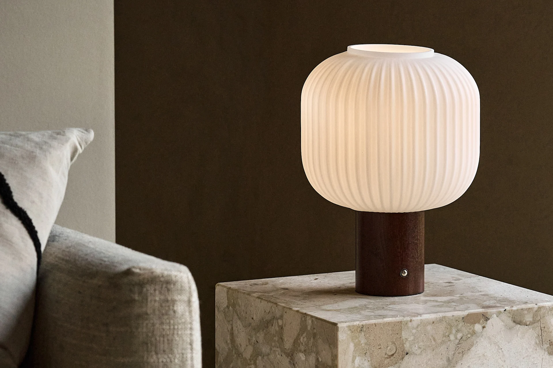 Hvit riflet bordlampe med trebunn på et marmorbord ved siden av en sofa.