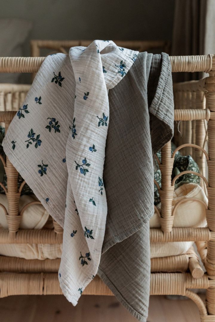 Blueberry Muslin-tepper fra Garbo&Friends, vist her hengende over en sengegavl, er allsidige tepper som kan brukes til mange ting, noe som gjør dem til perfekte babyshower-gaver.