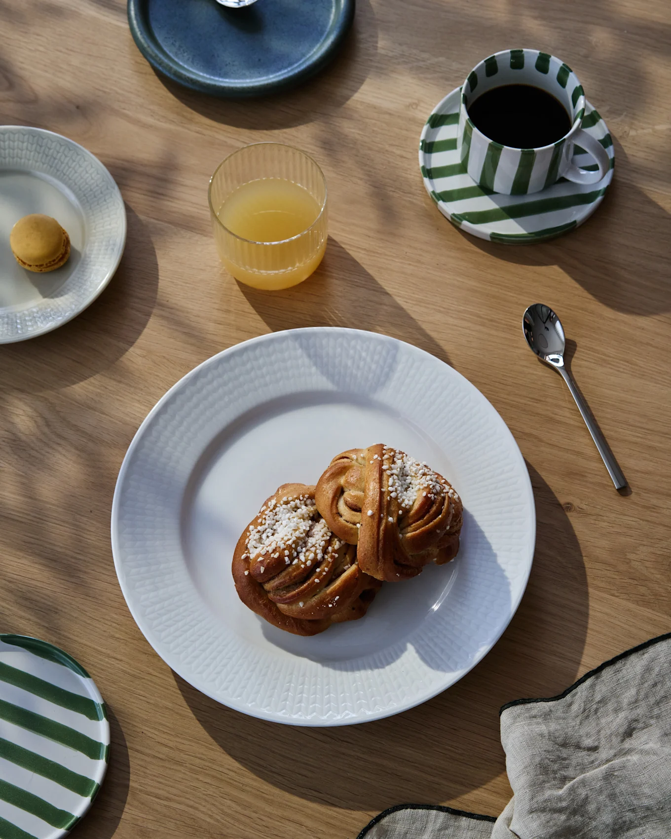 En frokostservering på et trebord med to kanelsnurrer, kaffe i en stripet kopp, appelsinjuice og en makron.