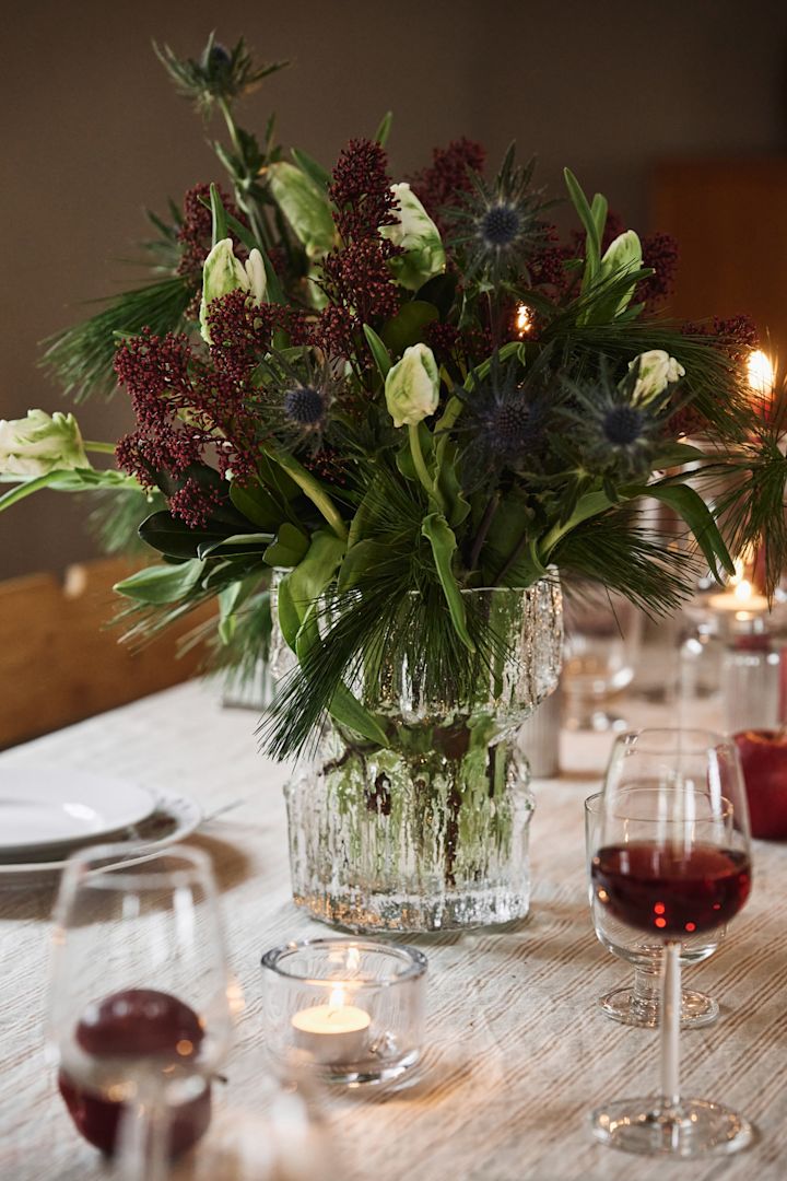 En teksturert glassvase med en vinterlig julebukett står på et enkelt julebord. 